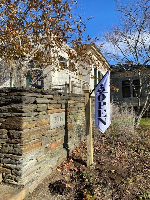 a flag reading "open" is displayed outside a stone building with the address 2013 engraved on a wall. trees with autumn leaves and a clear blue sky are visible.