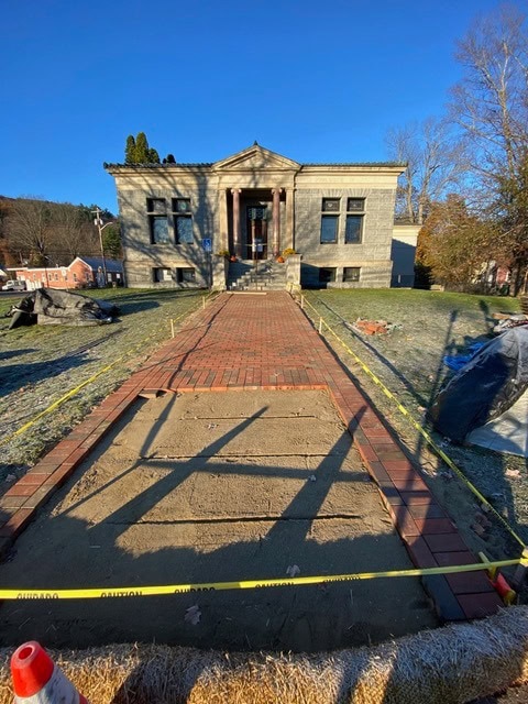 a brick pathway under construction leads to the entrance of a stone building; caution tape blocks off the unfinished section.