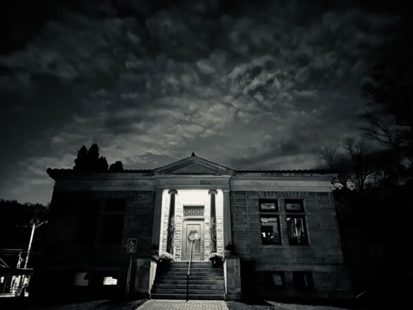 a historic stone building with columns is illuminated at night, with dramatic clouds in the sky above.