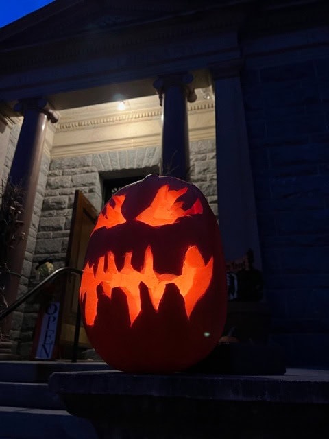 a carved pumpkin with a jagged, menacing face is lit from within and sits on stone steps outside a building at night.