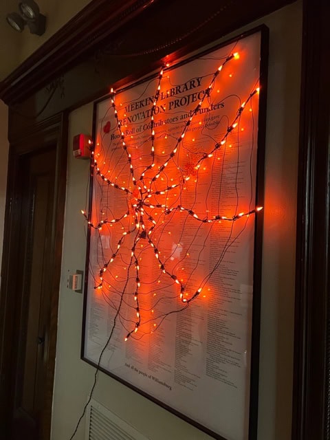 a poster on the wall is decorated with orange string lights arranged in a spider web pattern.