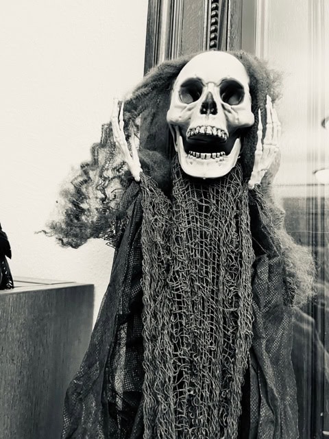a skeleton decoration with wild hair and tattered cloth stands with its hands raised near its head, displayed indoors.