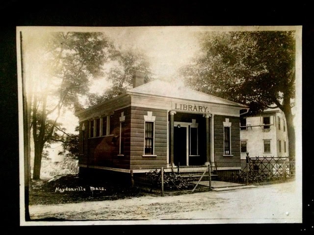 black and white photo of a small, historic library building labeled "library" in haydenville, massachusetts, surrounded by trees and a dirt road.