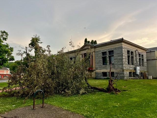 a large fallen tree lies on the lawn in front of an old stone building under a cloudy sky.