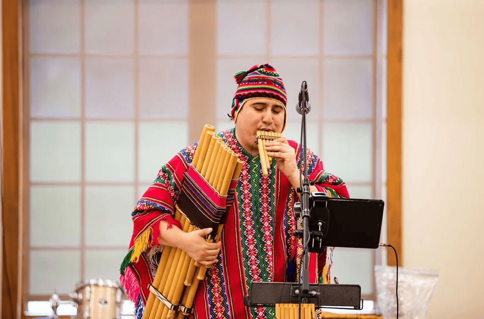 a person wearing a traditional colorful poncho and knit cap plays a pan flute.