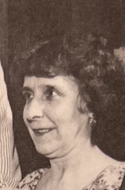 black and white photo of a woman with short, curly hair, wearing earrings and a patterned top, looking slightly to the side.