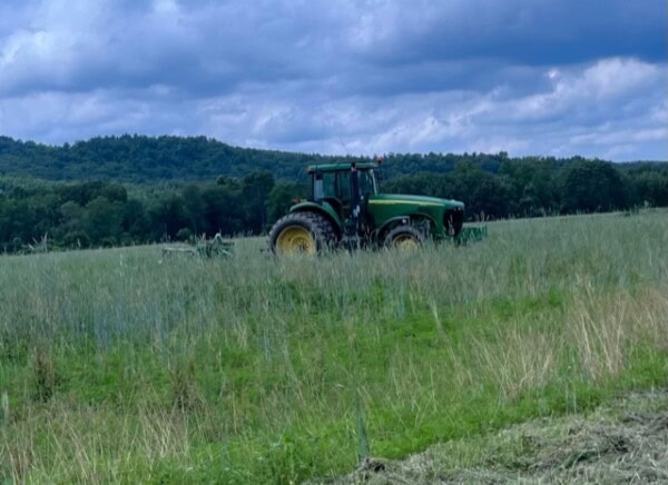 a green tractor is positioned in the middle of a grassy field with trees and cloudy sky in the background.