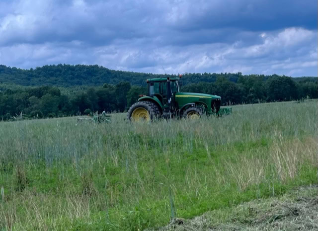 a green tractor is positioned in the middle of a grassy field with trees and cloudy sky in the background.