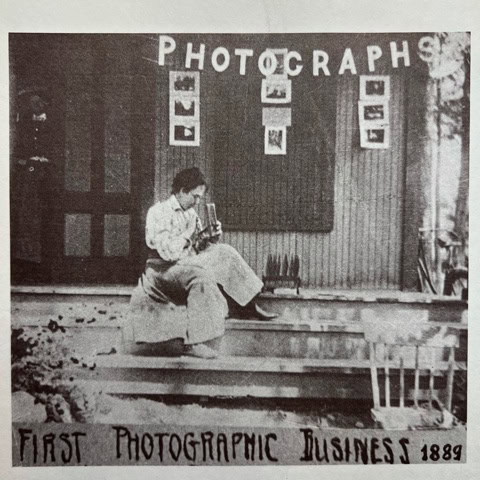 black and white photo of a person seated on steps outside a building labeled