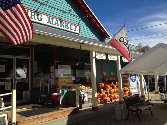 a small market with a teal exterior displays pumpkins outside, with american and ohio flags and a canopy covering benches in front.