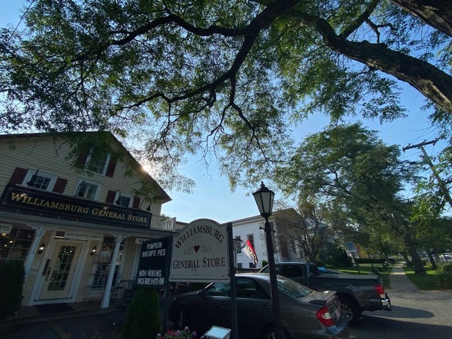 street view of williamsburg general store with its sign, a parked car, trees overhead, and a clear sky in the background.