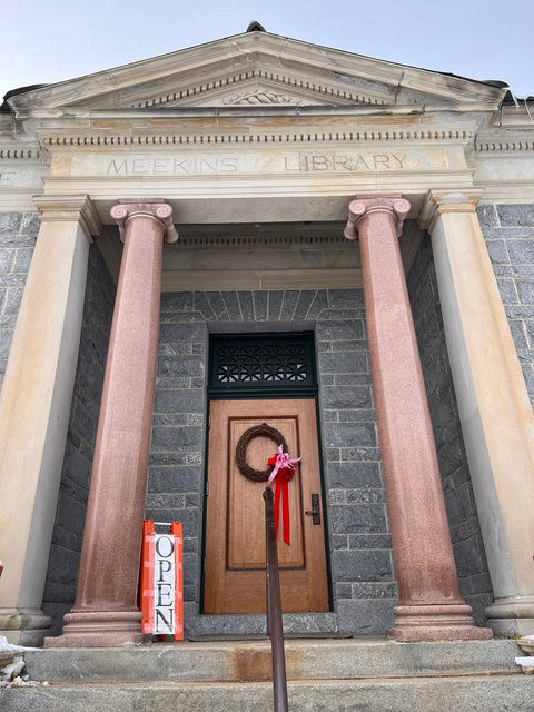 front entrance of meekins library with two large columns, a wreath on the door, and an "open" sign on the steps.