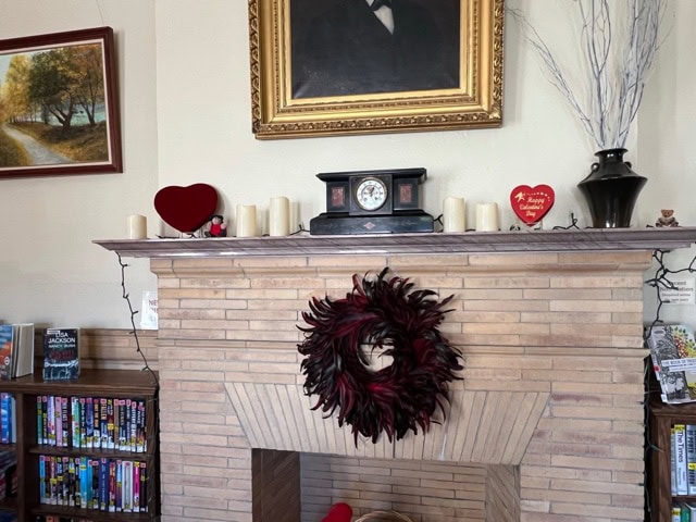 a fireplace with a decorative wreath, candles, and a clock on the mantel. bookshelves and framed paintings are on the wall, with a large portrait hanging above the mantel.
