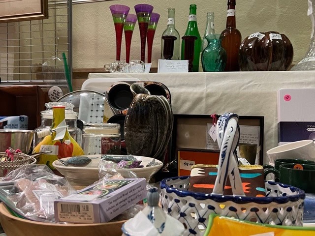 a variety of vintage glassware, ceramic dishes, bottles, and decorative items displayed on a table at a thrift or antique store.