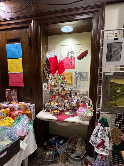 a small holiday market display with stockings, ornaments, toys, and various decorations arranged on tables and shelves in a wooden alcove.