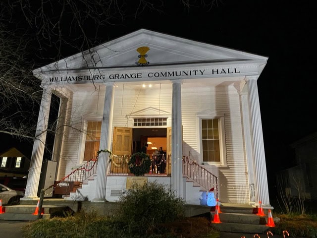 williamsburg grange community hall at night, lit from the front with holiday wreaths on the doors and traffic cones along the sidewalk.