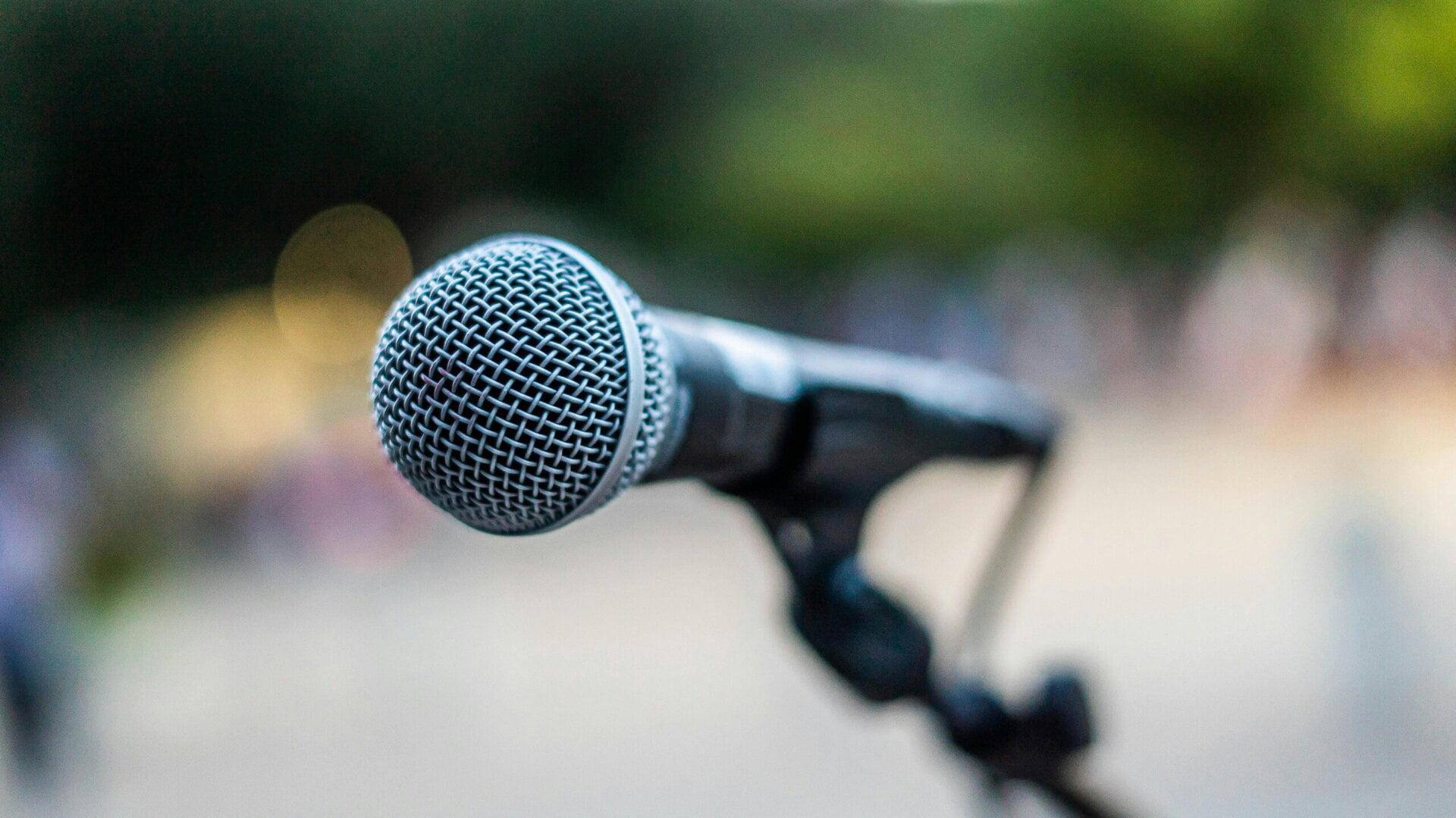 a close up of a microphone on a stand, with a blurred outdoor background.