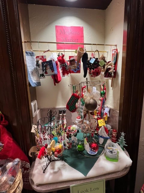 a display of assorted christmas ornaments and stockings hangs and sits on shelves under a sign reading "meekins market." small holiday figurines and decorations are arranged below.