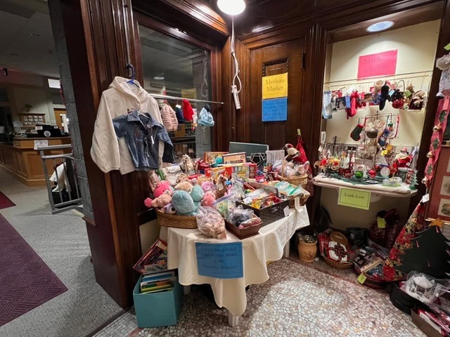 a display of toys, stuffed animals, books, and various holiday decorations arranged on tables in a library or store corner.