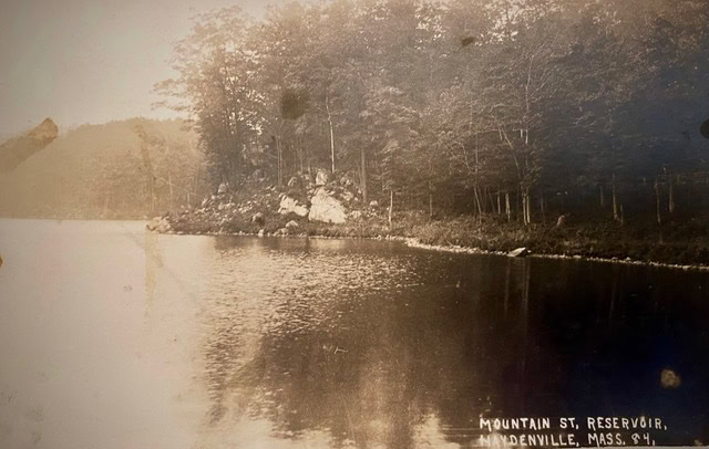 black and white photo of a calm reservoir bordered by trees and rocks, labeled "mountain st. reservoir, andenville, mass." in the lower right corner.