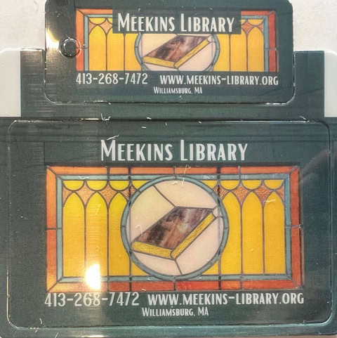 two meekins library cards with a stained glass book design, library name, contact info, website, and williamsburg, ma location printed on them.
