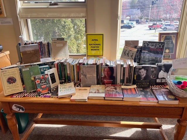 a display table in a library features a variety of poetry books and anthologies for national poetry month, with a sign reading "april national poetry month" in the background.