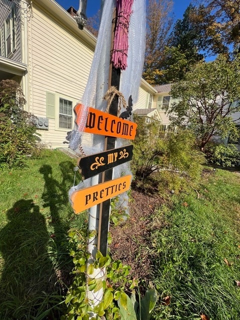 a halloween themed sign reading "welcome my pretties" is attached to a pole in a grassy front yard with a house in the background.