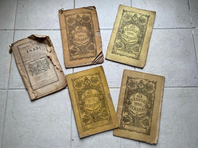 five vintage “old farmer’s almanac” booklets from the early 1900s are spread out on a tiled floor, some with worn and damaged covers.