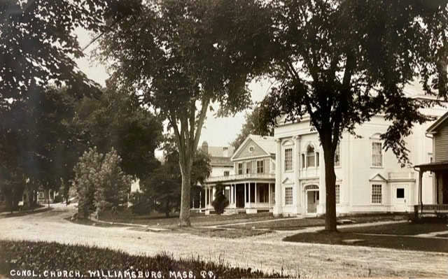 black and white photo of a street in williamsburg, massachusetts, featuring the congregational church and nearby houses with large trees lining the road.