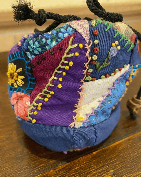 a small drawstring pouch made from multicolored patchwork fabric, decorated with various hand stitched embroidery designs.