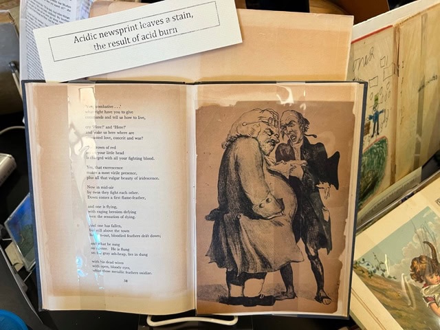 an open book displays an illustration of two men arguing and a page of text; a sign above reads, "acidic newsprint leaves a stain, the result of acid burn.