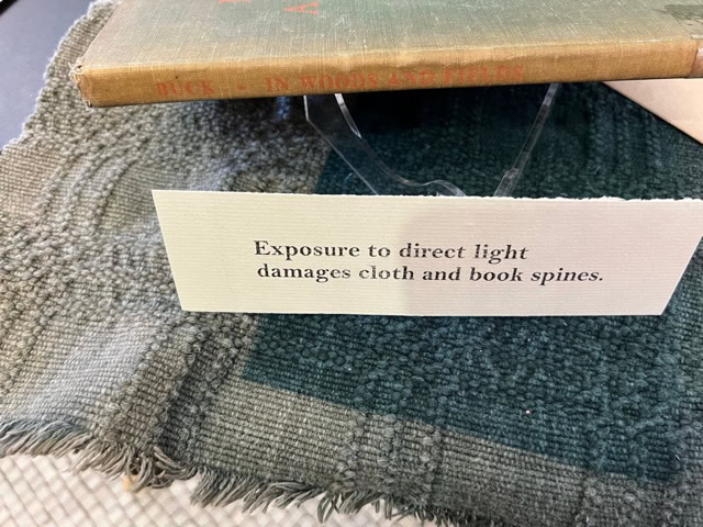 a sign reads, "exposure to direct light damages cloth and book spines," placed in front of a cloth covered book.