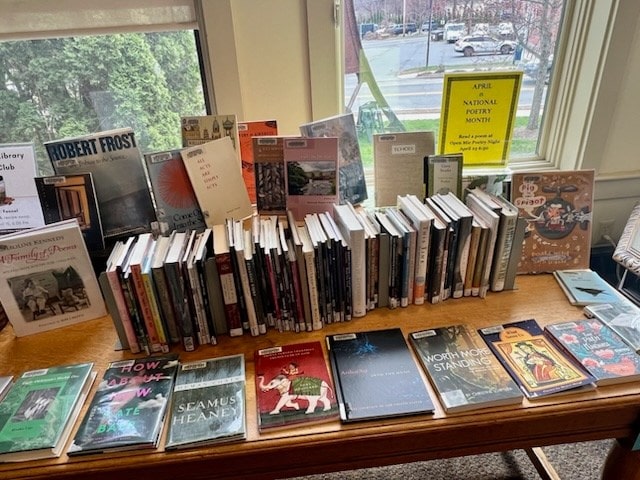 a display table in a library features a variety of poetry books and pamphlets, with a sign in the background marking national poetry month in april.