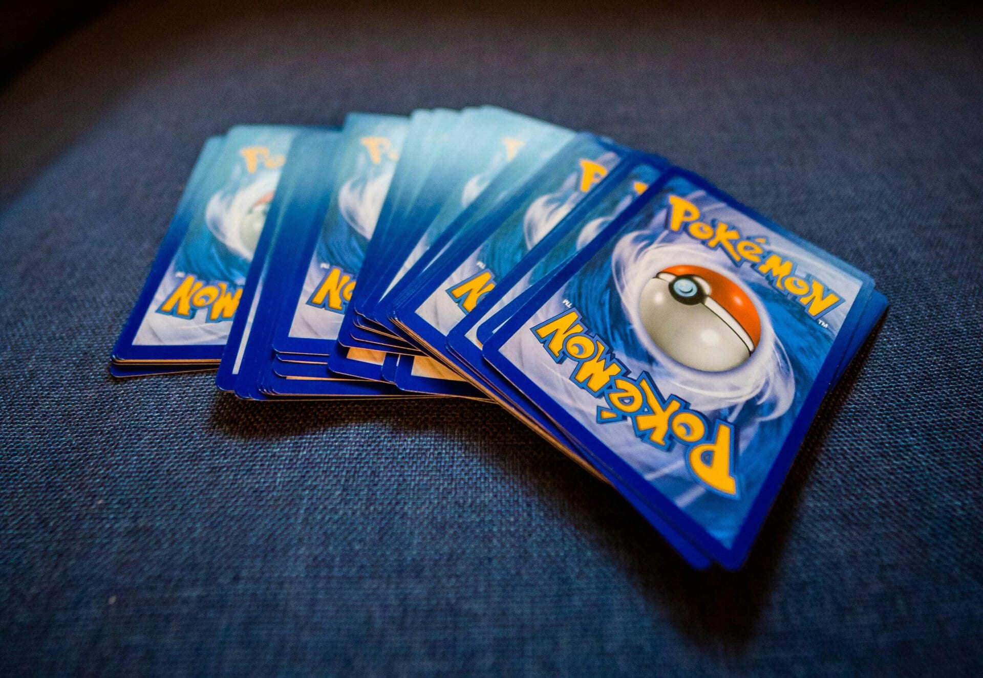 a fan of pokémon trading card game cards fanned out on a dark blue fabric surface.