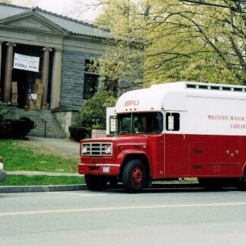 a red and white bookmobile labeled "western massachusetts library" is parked in front of a stone building with columns and a sign that says "media" near the entrance.