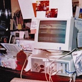 a vintage desktop computer setup with a crt monitor, tower, keyboard, and scattered papers and photographs in the background.