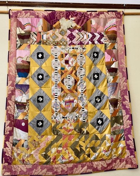 a colorful patchwork quilt featuring geometric patterns in yellow, gold, gray, pink, and purple fabrics, bordered with a floral print.