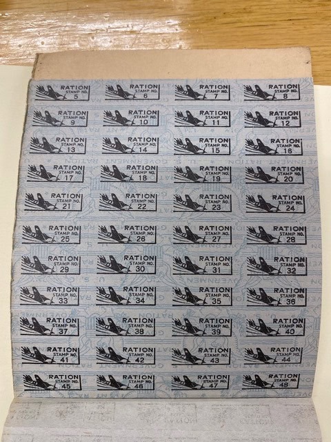a sheet of vintage ration coupons numbered 9 to 45, each labeled "ration" with an eagle emblem and crossed tools, attached to a booklet on a wooden surface.