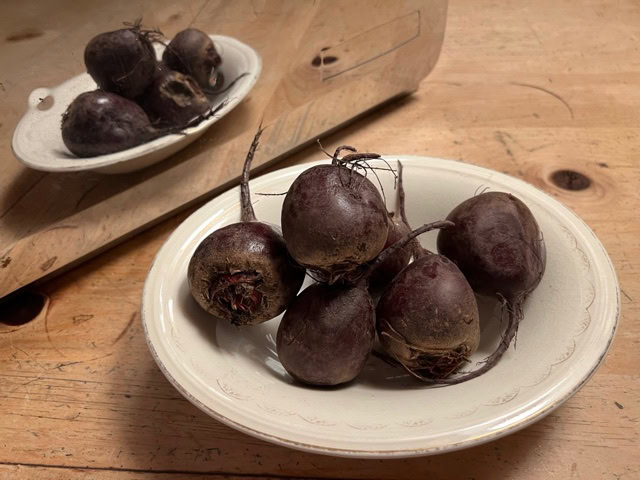 a white plate with several raw beets sits on a wooden table, with their reflection visible in a nearby mirror.