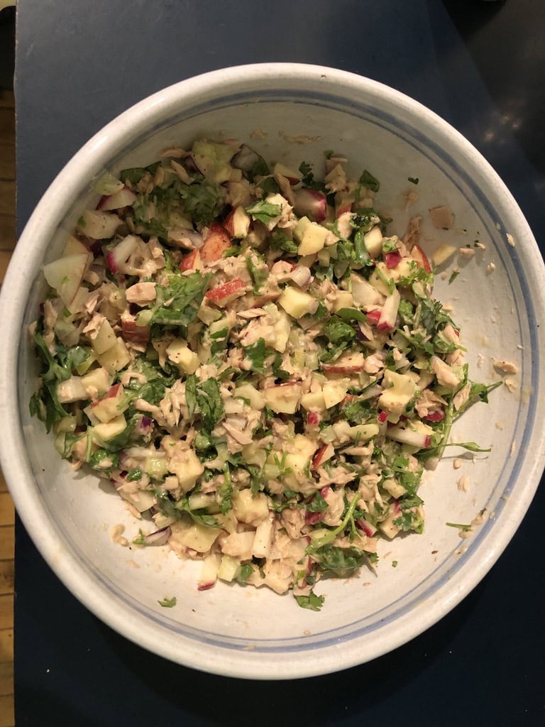 a large bowl filled with a chopped salad containing vegetables, herbs, and possibly tuna or chicken, mixed together on a dark surface.