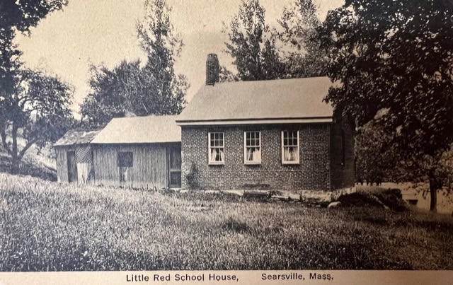a small brick schoolhouse with a chimney stands next to a wooden outbuilding, surrounded by trees and grass. the caption reads: little red school house, searsville, mass.
