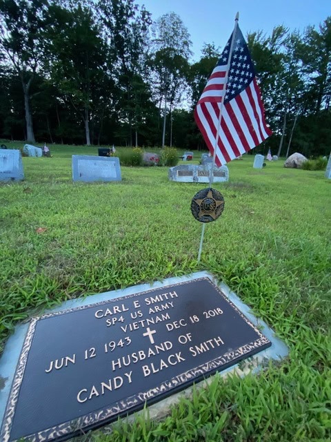 a gravestone for carl e. smith, a us army vietnam veteran, with an american flag and cemetery markers in the background.