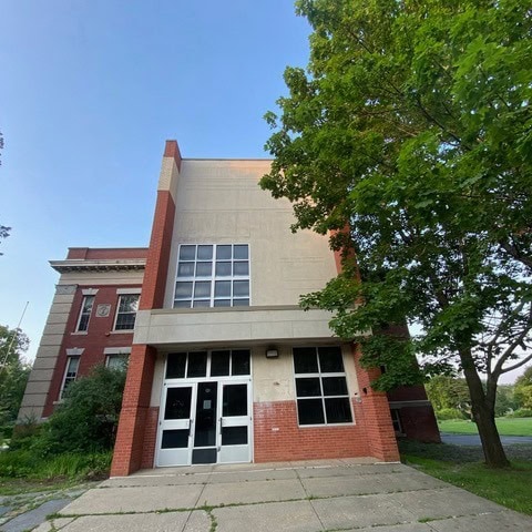 a two story brick and concrete school building with large windows and a tree to the right, under a clear sky.