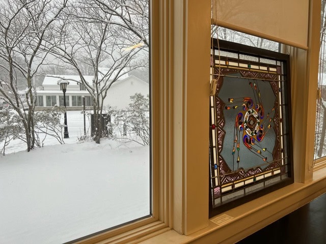 a snowy scene outside a window, with bare trees and buildings visible, and a colorful stained glass panel hanging in the window.