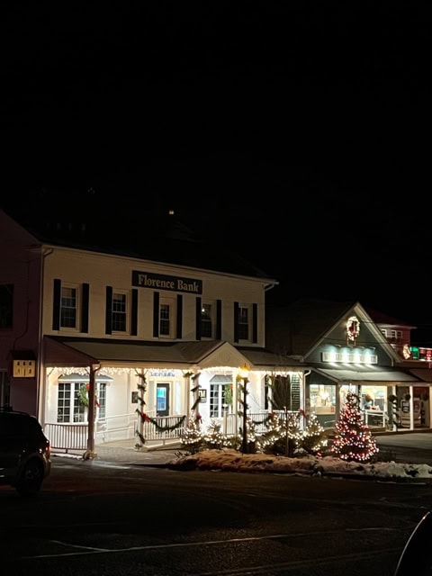 florence bank building decorated with holiday lights at night, with a lit christmas tree and some snow on the ground.