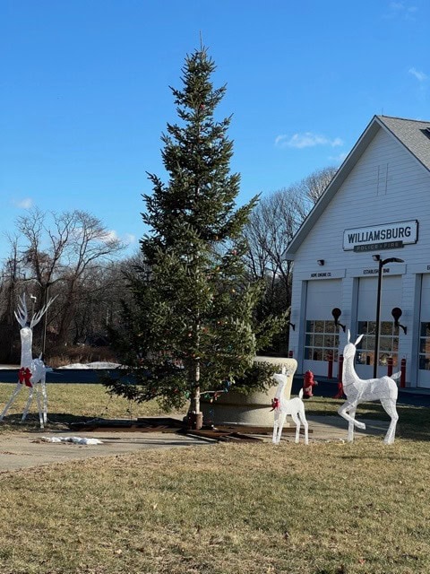 a decorated evergreen tree and three white wire frame reindeer stand in front of a building labeled "williamsburg" on a sunny day.
