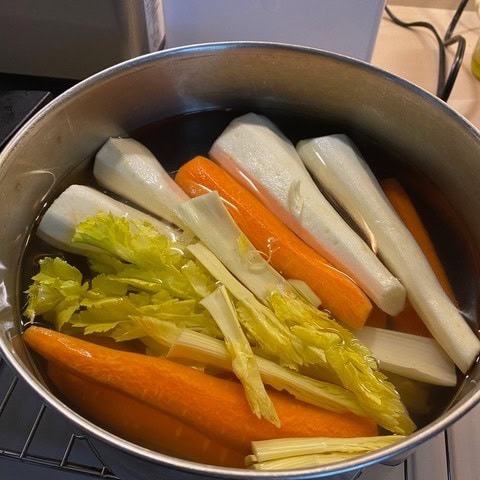 a pot of water containing peeled carrots, parsnips, and celery stalks, prepared for cooking.