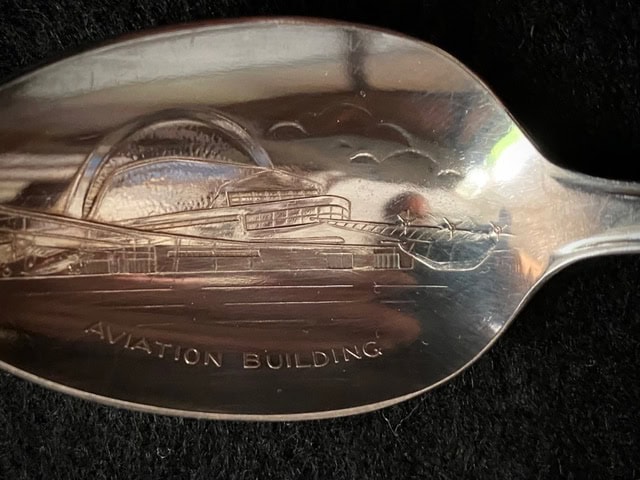 a metal spoon engraved with an image of a building and the words "aviation building" on the bowl, set against a black background.