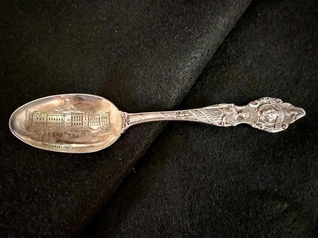 an ornate silver souvenir spoon featuring an engraved building on the bowl and a detailed decorative handle with a woman's portrait.