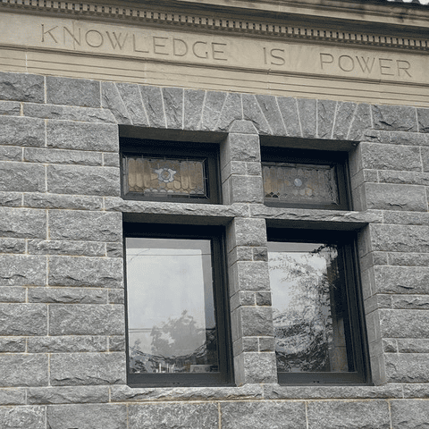 stone building facade with two windows and a carved inscription above them that reads, "knowledge is power.